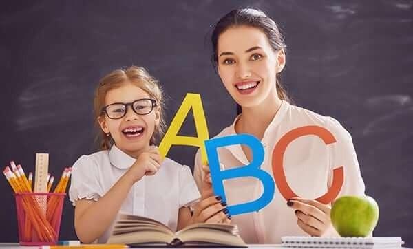 a female teacher and a student holding up a wooden A, B and C while smiling in a classroom