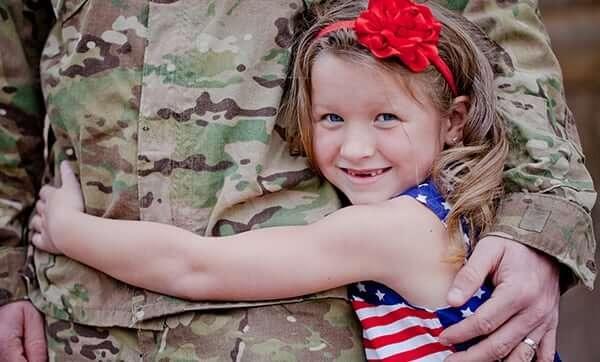 a little girl wearing red,white and blue attire hugging a soldier